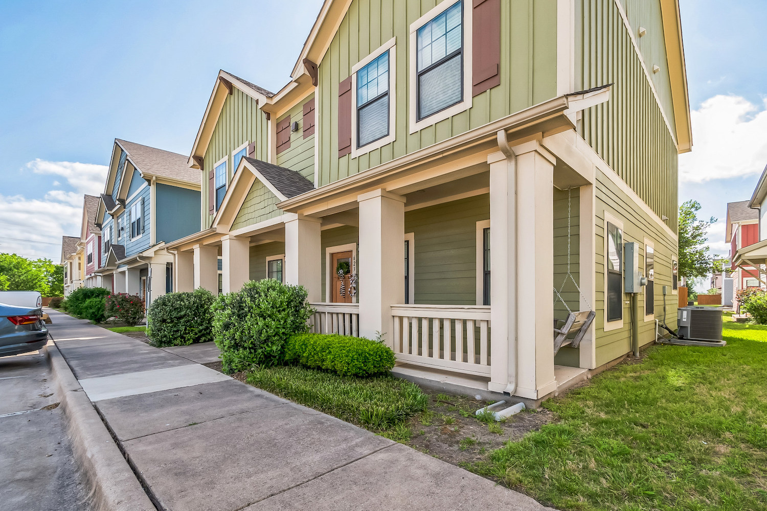 A row of modern, colorful townhouses with front porches, green lawns, and shrubs beside a sidewalk on a sunny day—perfect for TAMU off campus housing.