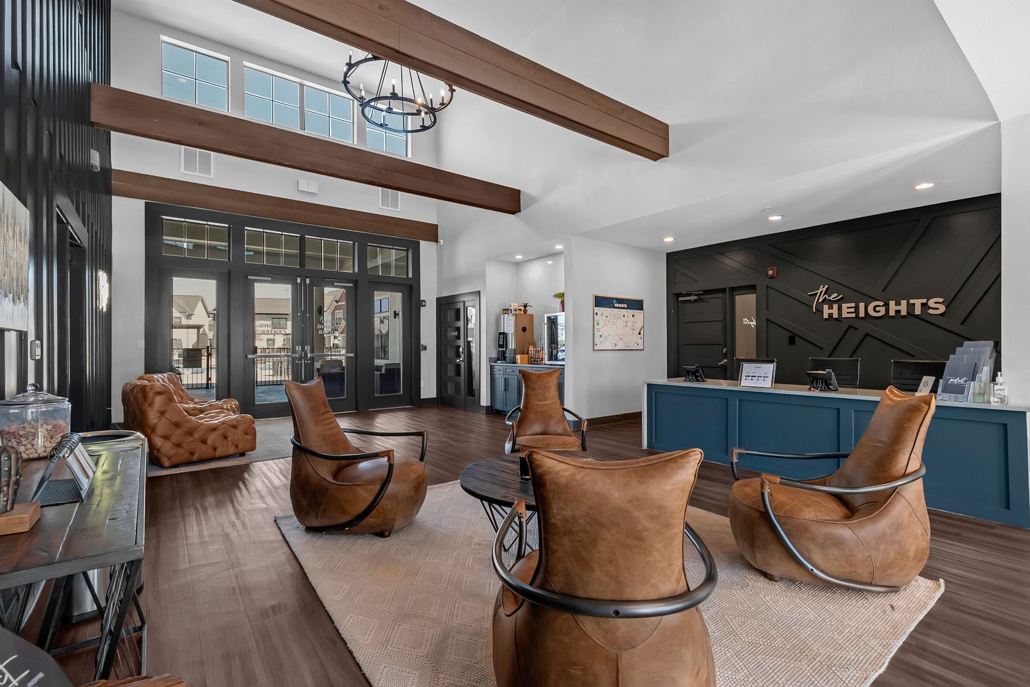 Modern apartment leasing office with high ceilings, exposed wooden beams, leather chairs, and a blue front desk labeled The Heights. Ideal for TAMU off campus housing, its large windows fill the welcoming space with natural light.