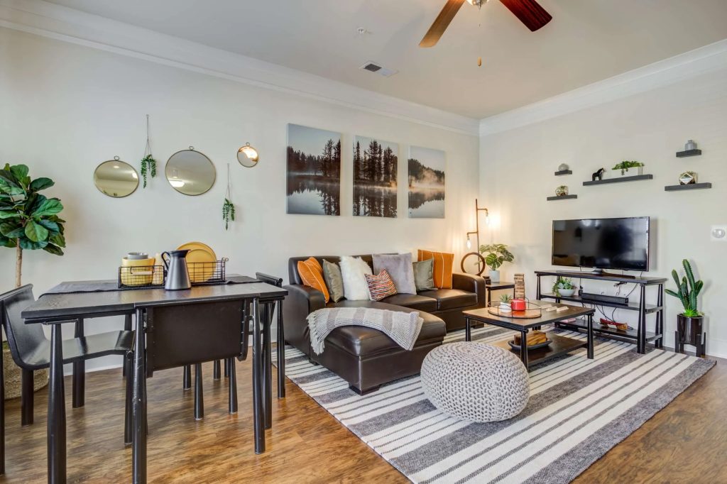 Furnished living room at Redpoint College Station featuring a sectional sofa, dining area, TV and wood-style flooring.