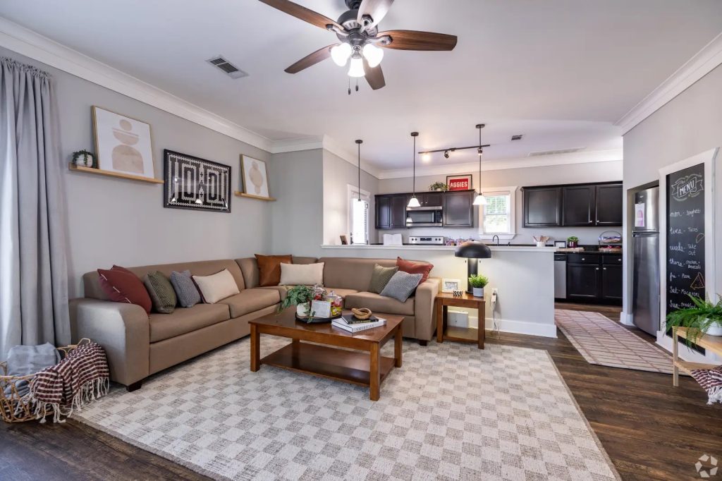 Open-concept living room and kitchen inside a furnished cottage-style apartment at The Cottages of College Station.