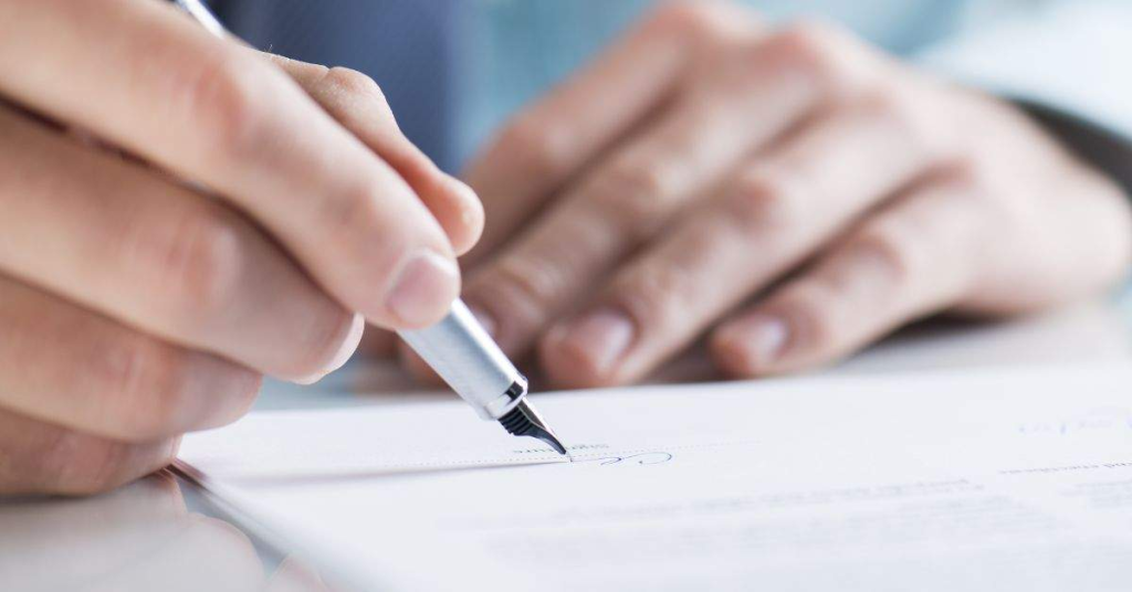 Someone signing their name on a paper with a pen.
