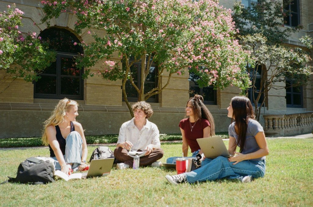 A group of friends sitting on the grass outside of a building at Texas A&M.